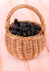 Ripe mulberries in wicker basket on wooden background