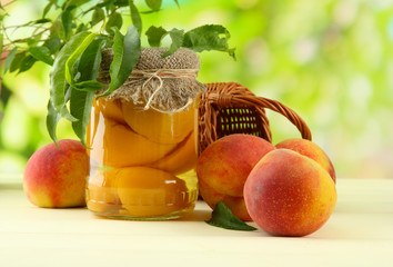 Jar of canned peaches and fresh peaches on wooden table,