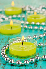 Lighted candles with beads on green background