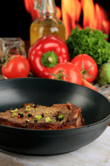 Piece of fried meat on pan on wooden table on fire background