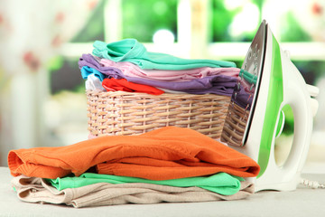 Steam iron and wicker basket with clothes, on bright background