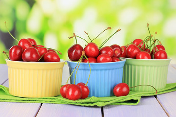 Cherry berries in bowls on wooden table on bright background