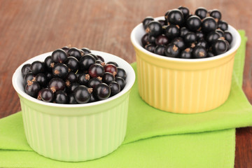 Fresh black currant in bowls on napkin on wooden background