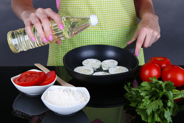 Hands cooking marrows in pan on gray background