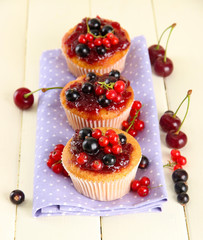 Tasty muffins with berries on white wooden table