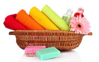 Colorful towels, cosmetics bottles and soap in basket, isolated