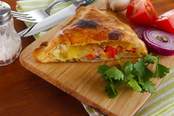 Pizza calzone on wooden board on napkin on wooden table