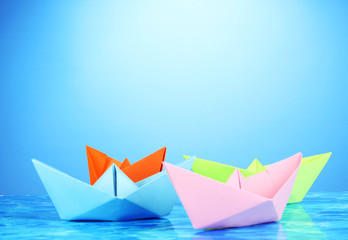 Paper ships of different colors on water background