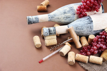 Fototapeta na wymiar Old bottles of wine, grapes and corks on brown background