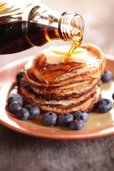Close-up of pouring maple syrup on stack of pancakes.