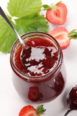 Glass with strawberry jam and fresh strawberries.