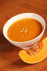 Bowl with pumpkin soup and slice of fresh pumpkin