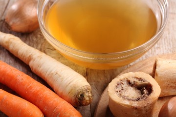 Bowl with beef broth, boiled bones and fresh vegetables.