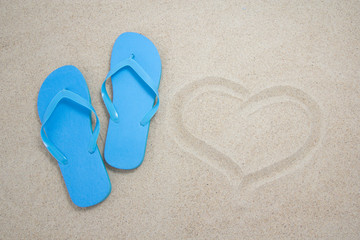 Fototapeta na wymiar blue flip flops and heart on sandy beach