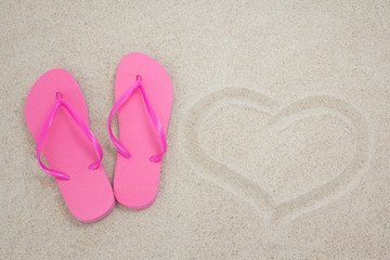Fototapeta na wymiar pink flip flops and heart on sandy beach