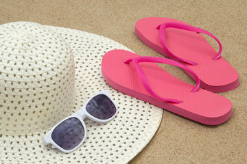 picture of pink flip flops, sunglasses and hat on beach sand