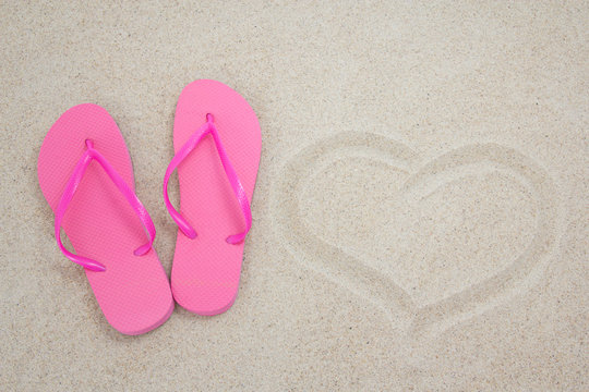 pink flip flops and heart on sandy beach