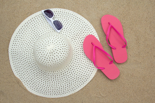 pink flip flops, sunglasses and hat on sandy beach