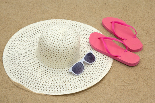 pink flip flops, sunglasses and hat on beach sand