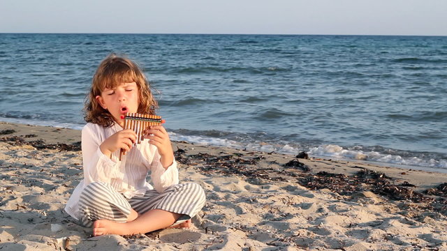 little girl play pan pipe on beach