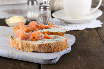 Fish sandwiches and cup of tea on cutting board on wooden table