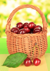 Cherry berries in wicker basket on table on bright background