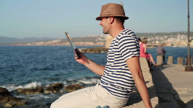 Happy man chatting on tablet computer by the sea