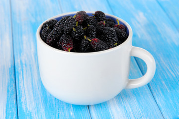Fototapeta na wymiar Ripe mulberries in cup on wooden background