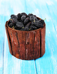 Ripe mulberries in bowl on wooden background