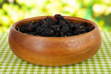 Ripe mulberries in bowl on table on bright background