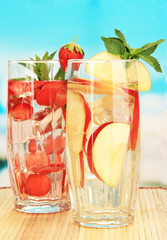 Glasses of fruit drinks with ice cubes on blue background