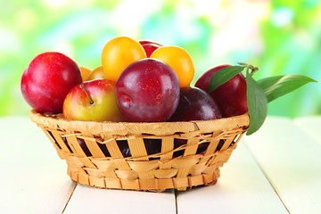 Ripe plums in basket on wooden table on natural background