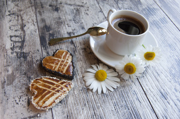 Cookies with a cup of coffee and flowers on the wooden table