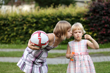 Dwie siostry z piłką dmuchają bańki mydlane.