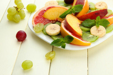 Assortment of sliced fruits on plate, on white wooden table