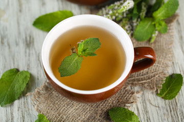 Cup of herbal tea with fresh mint flowers on wooden table
