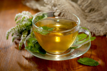 Cup of herbal tea with fresh mint flowers on wooden table