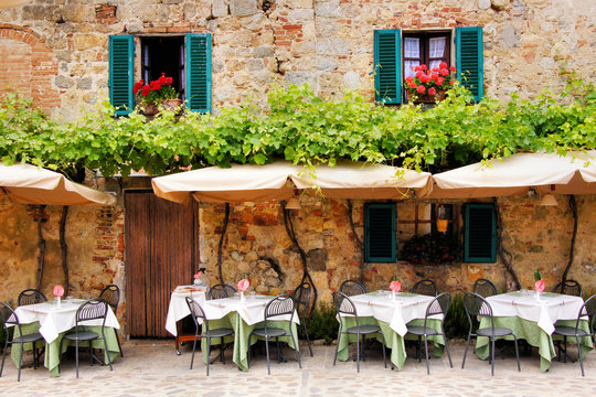 Fototapeta Cafe tables and chairs outside a stone building in Tuscany