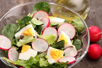 Bowl with egg and vegetable salad and ingredients on a table.