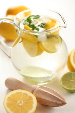 Jug of fresh lemonade with mint leaves and wooden squeezer.
