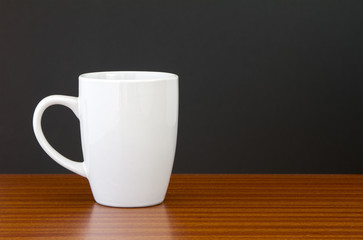White mug on dark wooden table with black wall