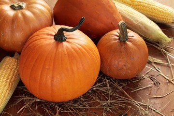 Pumpkins and corn on wooden background with straw.