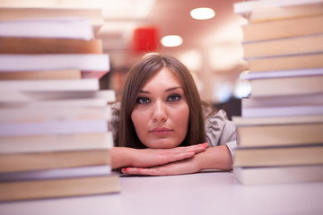 braunhaarige junge Dame schaut zwischen zwei Bücherstapel