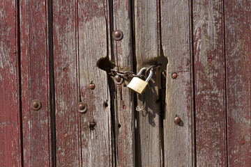 Candado y cadena sobre puerta despintada roja de madera