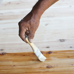 Hand holding a brush applying varnish paint on a wooden.