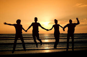 Group of happy people parting on the beach at sunrise