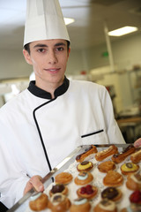 Young pastry cook holding tray of pastries