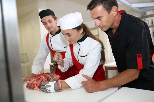 Professional butcher teaching students with meat cutting