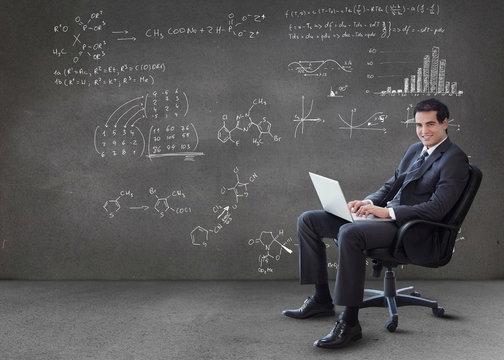 Businessman typing on his laptop with maths equations on wall