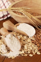 Wholegrain flour on wooden spoons, oats and corn.